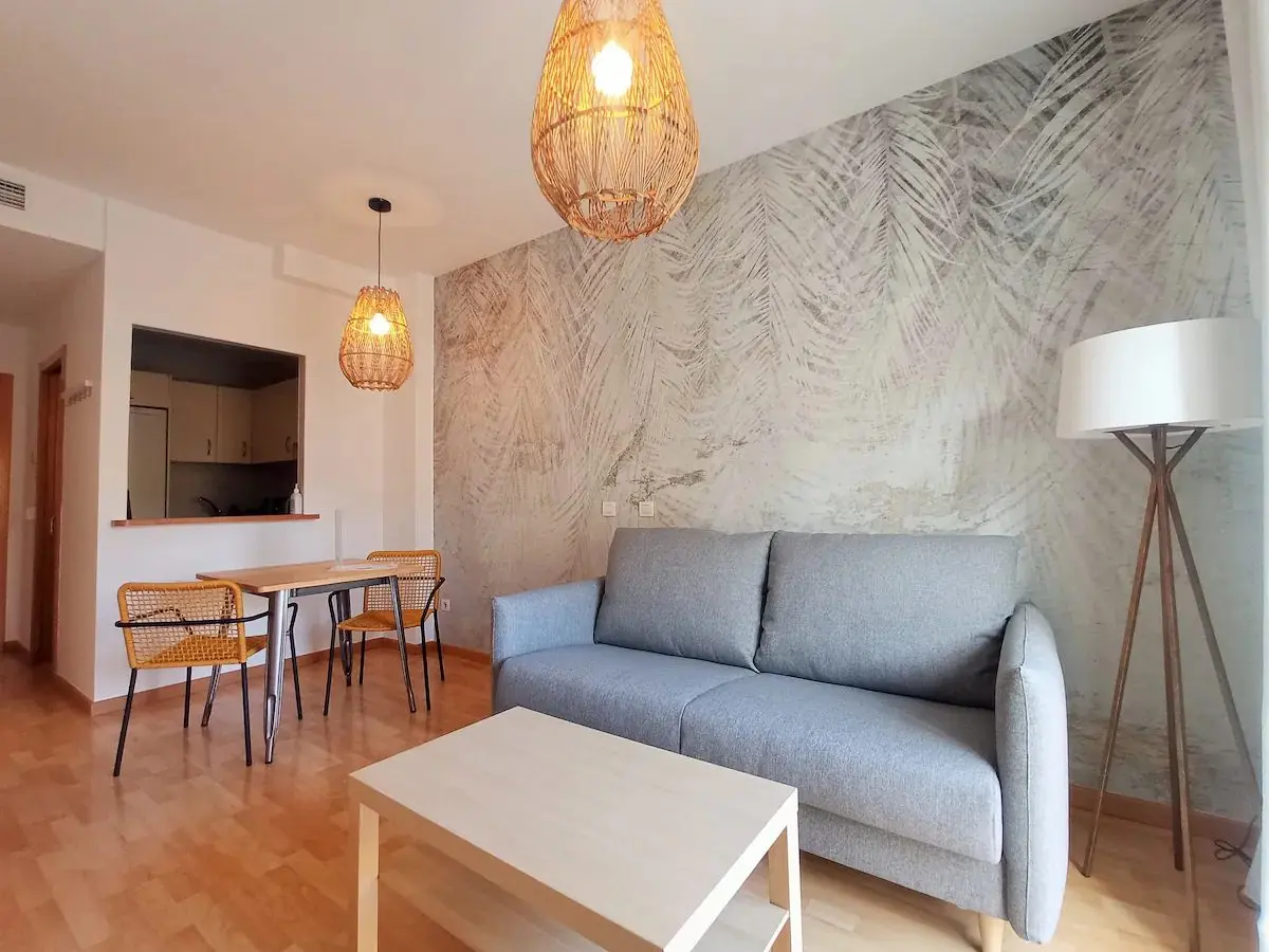 Salón luminoso con sofá gris y cocina abierta en un apartamento de LoftinMálaga